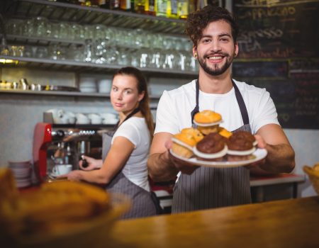 Portrait of waiter holding a plate of cup cake at counter Portrait of waiter holding a plate of cup cake at counter in café